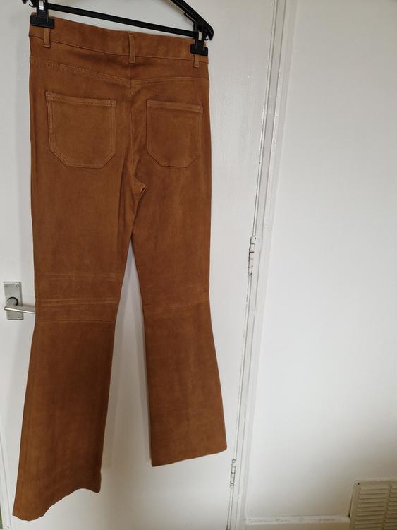 Brown flared trousers hanging on a black hanger over a white door. Back pockets visible.