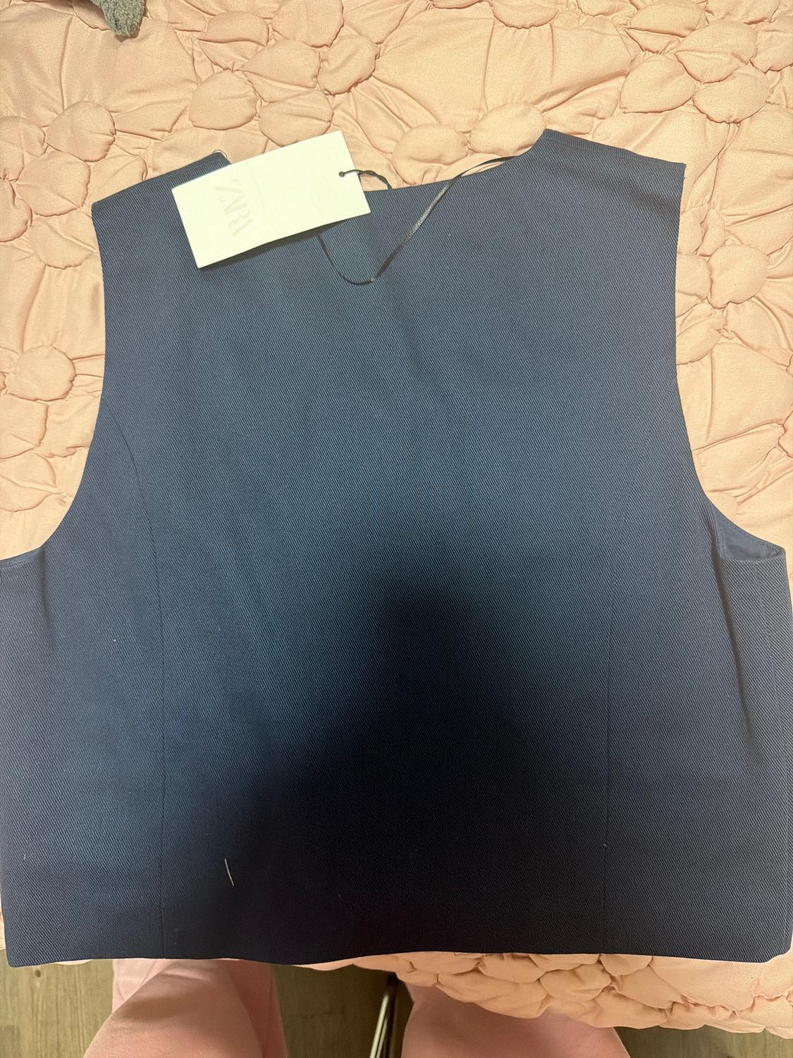 Blue sleeveless vest on a pink quilted comforter. White tag hanging from the collar.