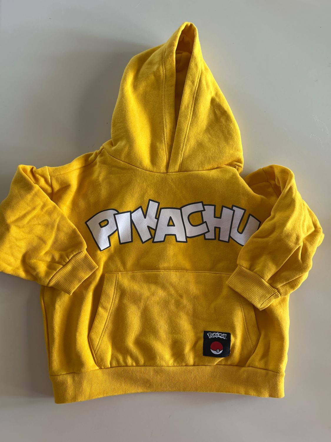 Yellow hoodie, "PIKACHU" text on the front and Pokémon label on the pocket. White background.