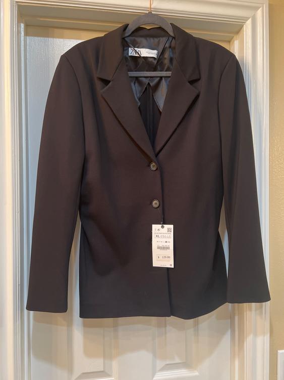Black suit jacket hanging on a door, with a visible tag indicating size XL and a price of $129.00.