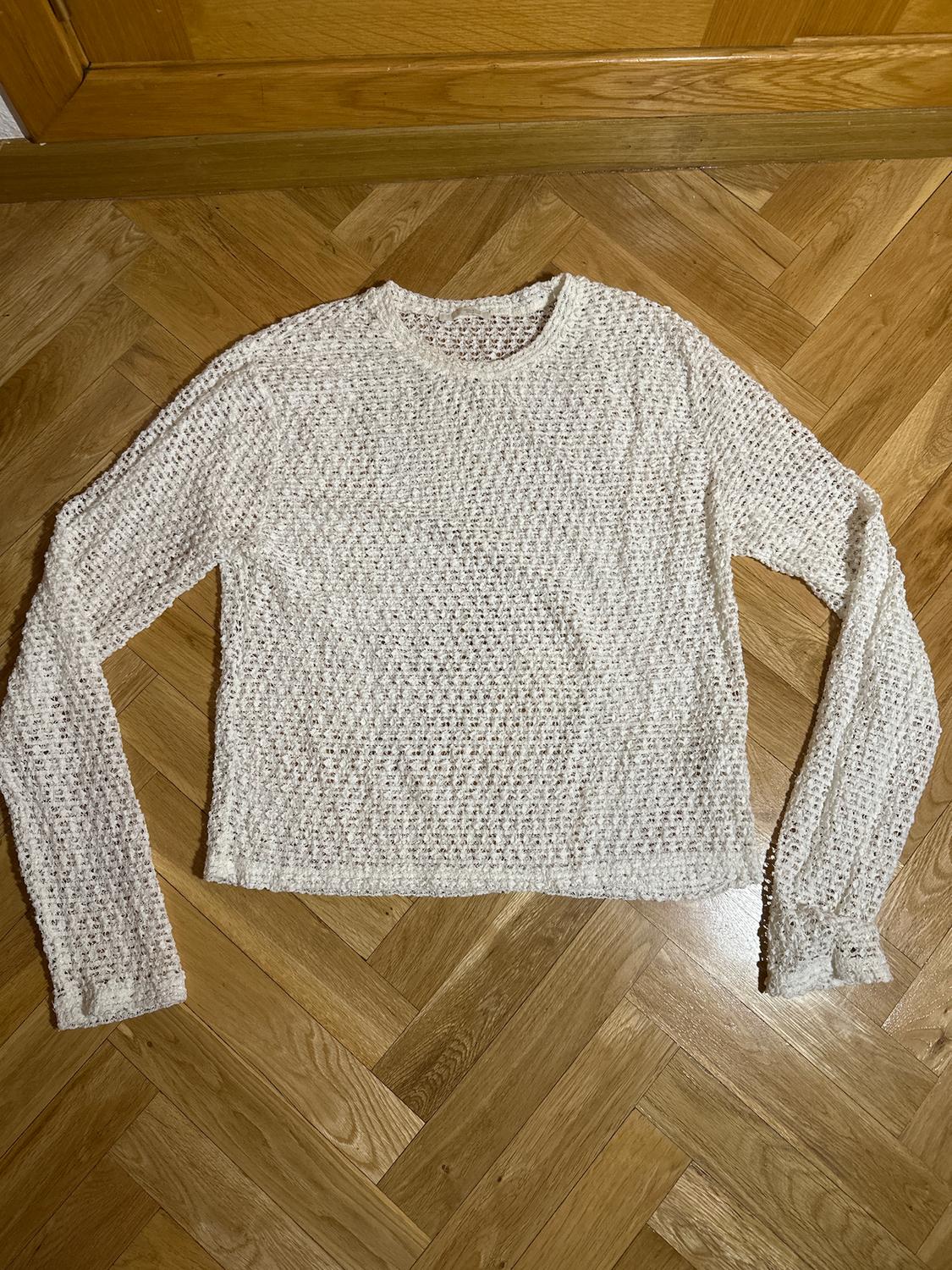 White open-knit jumper with long sleeves, placed on a light wooden floor.