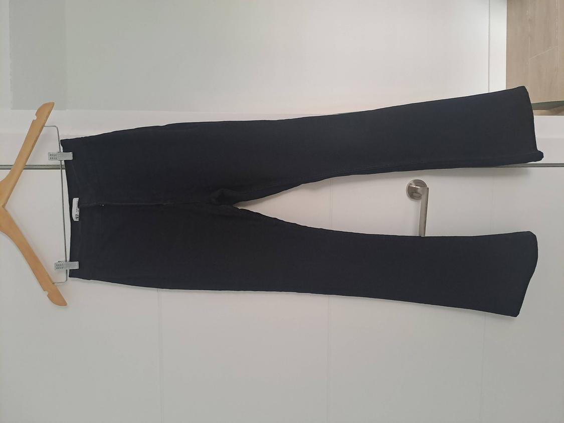 Dark trousers held by a wooden hanger, hung horizontally over a white door with a handle. Relaxed atmosphere.