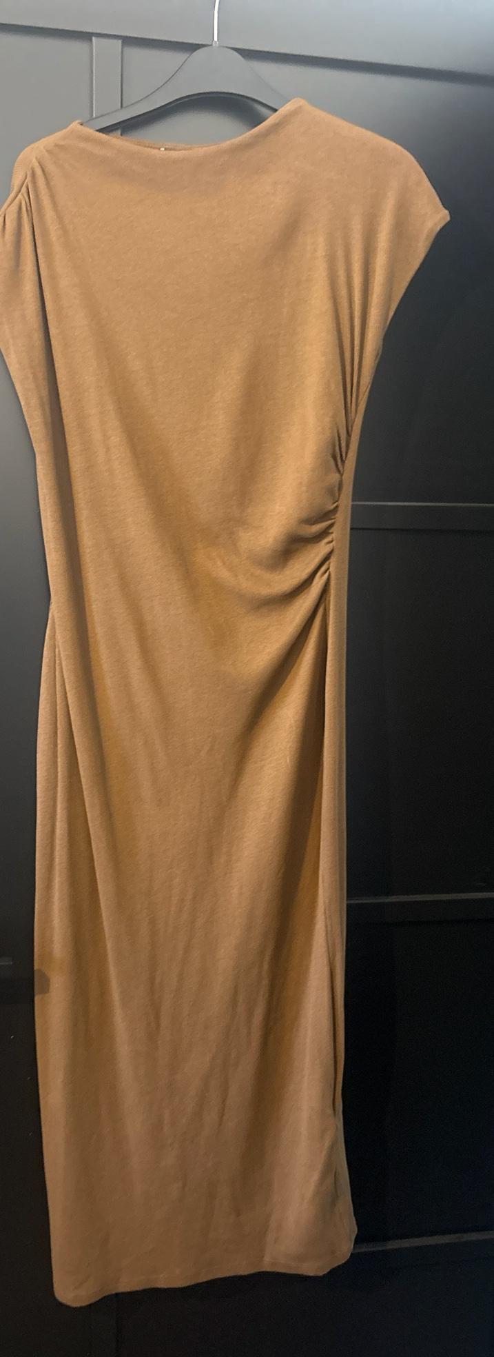 Camel sleeveless maxi dress with side gathering detail, hanging on a black hanger in front of a dark door.