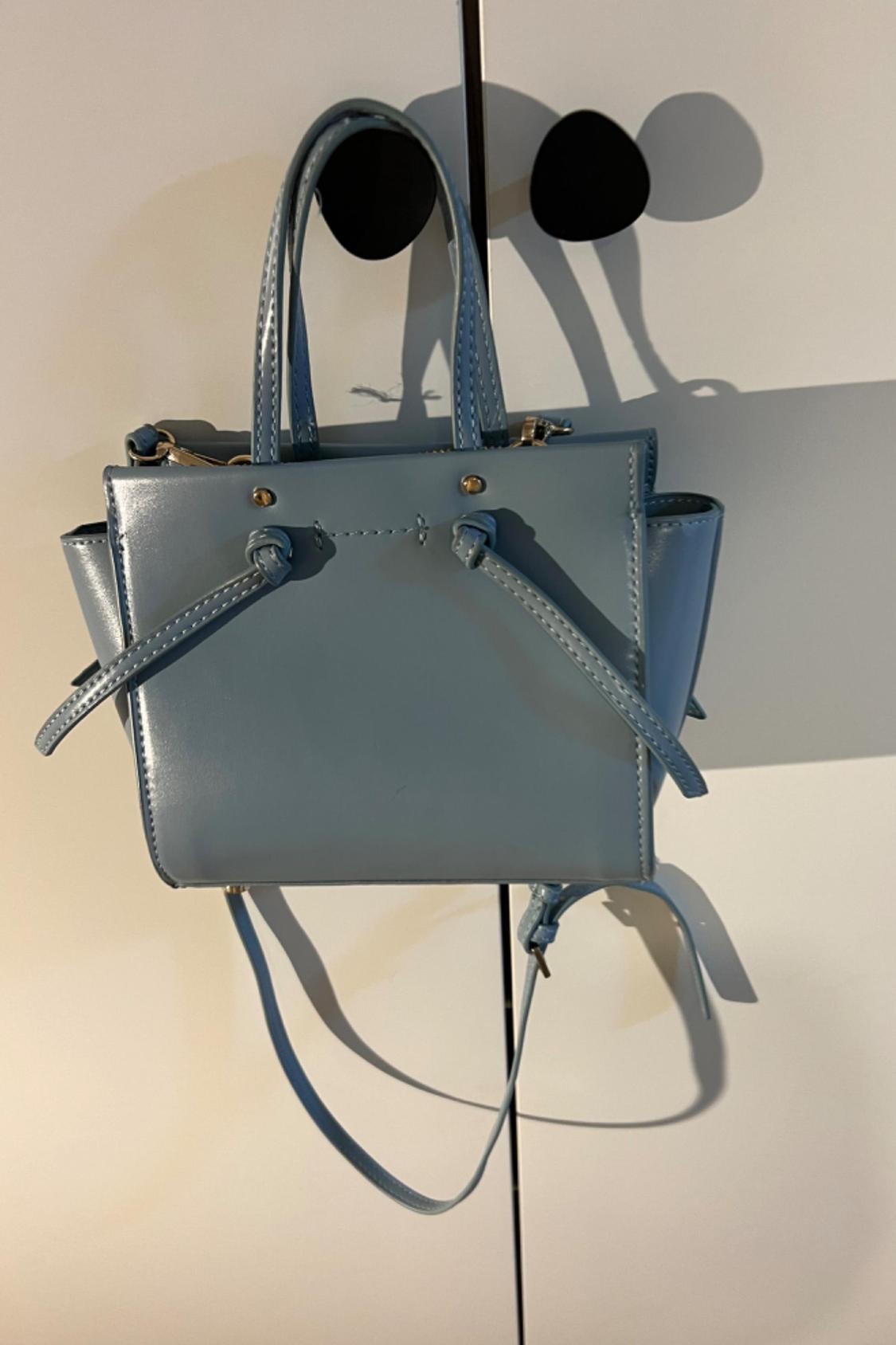 Front view of a blue bag with handles and an adjustable strap.