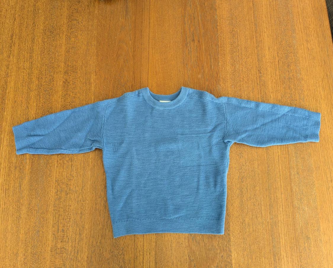 Long-sleeved blue sweater spread out on a wooden table.