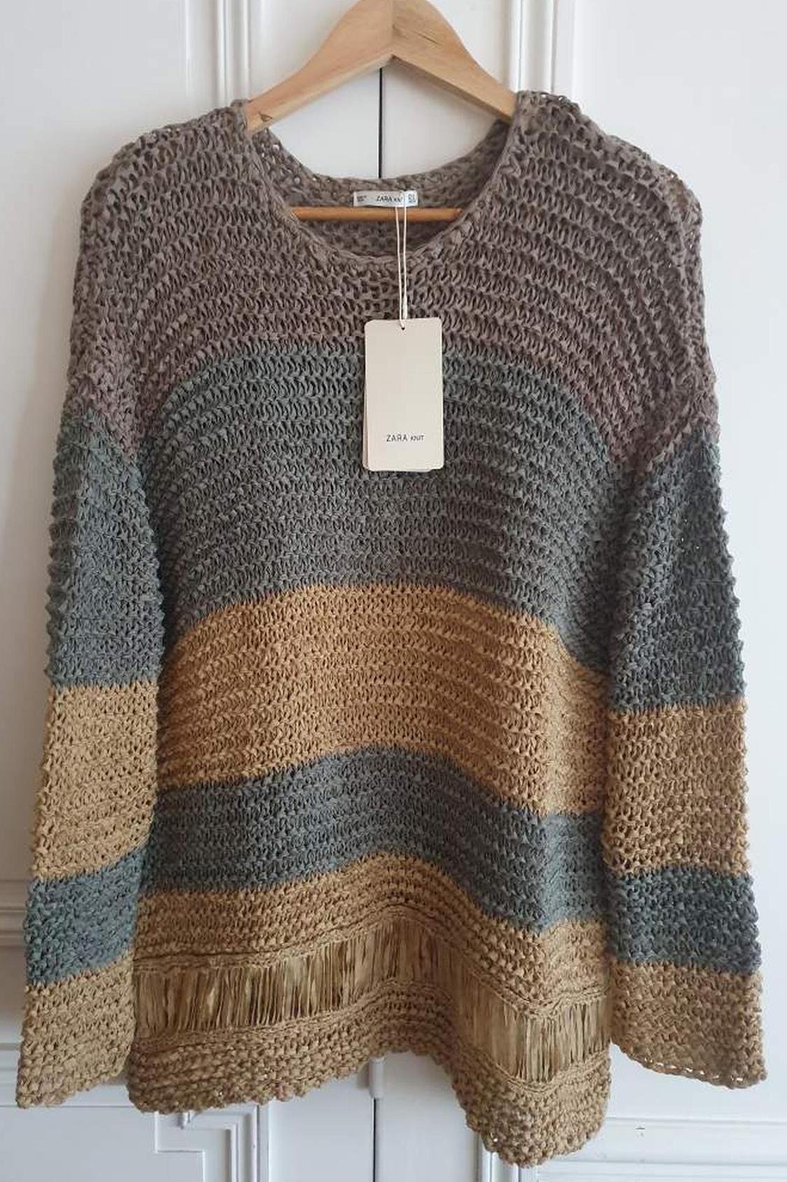 Front view of multicoloured knitted jumper with label, with brown and grey stripes and fringe detail on the edge.