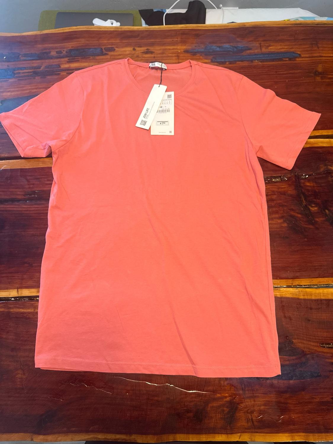 Coral short-sleeved basic t-shirt on a wooden table. Includes labels with the text JOIN LIFE and €7.