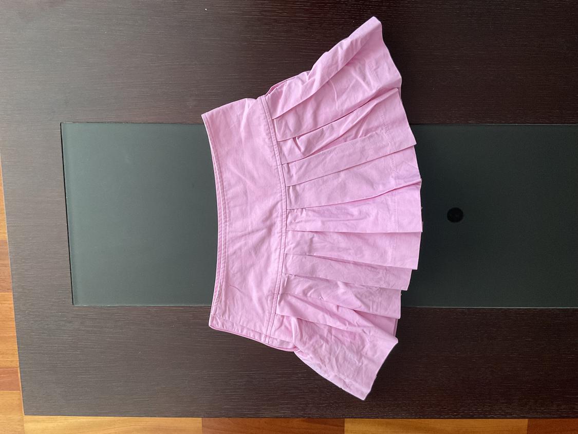 Short pink pleated skirt on a dark wooden table and black glass.