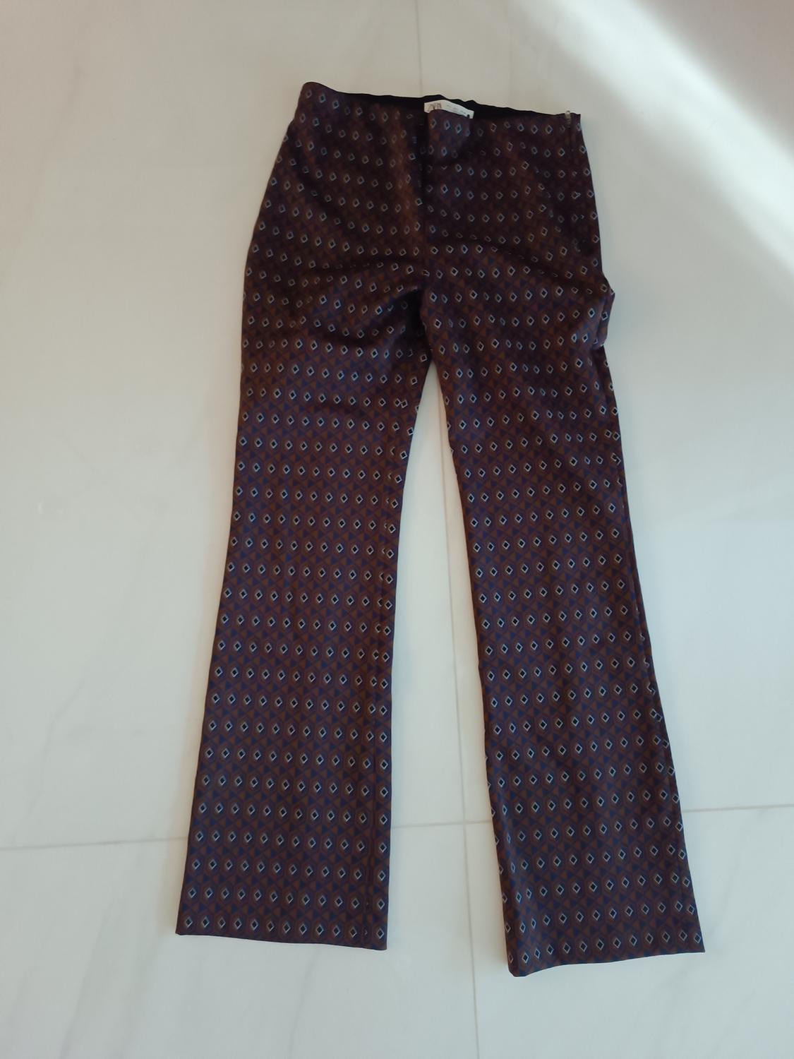 Brown fabric trousers with a small blue and white diamond pattern, placed on a light floor.