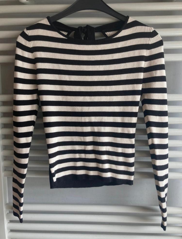 Black and white horizontal striped jumper hanging on a black hanger against a grey slatted background.
