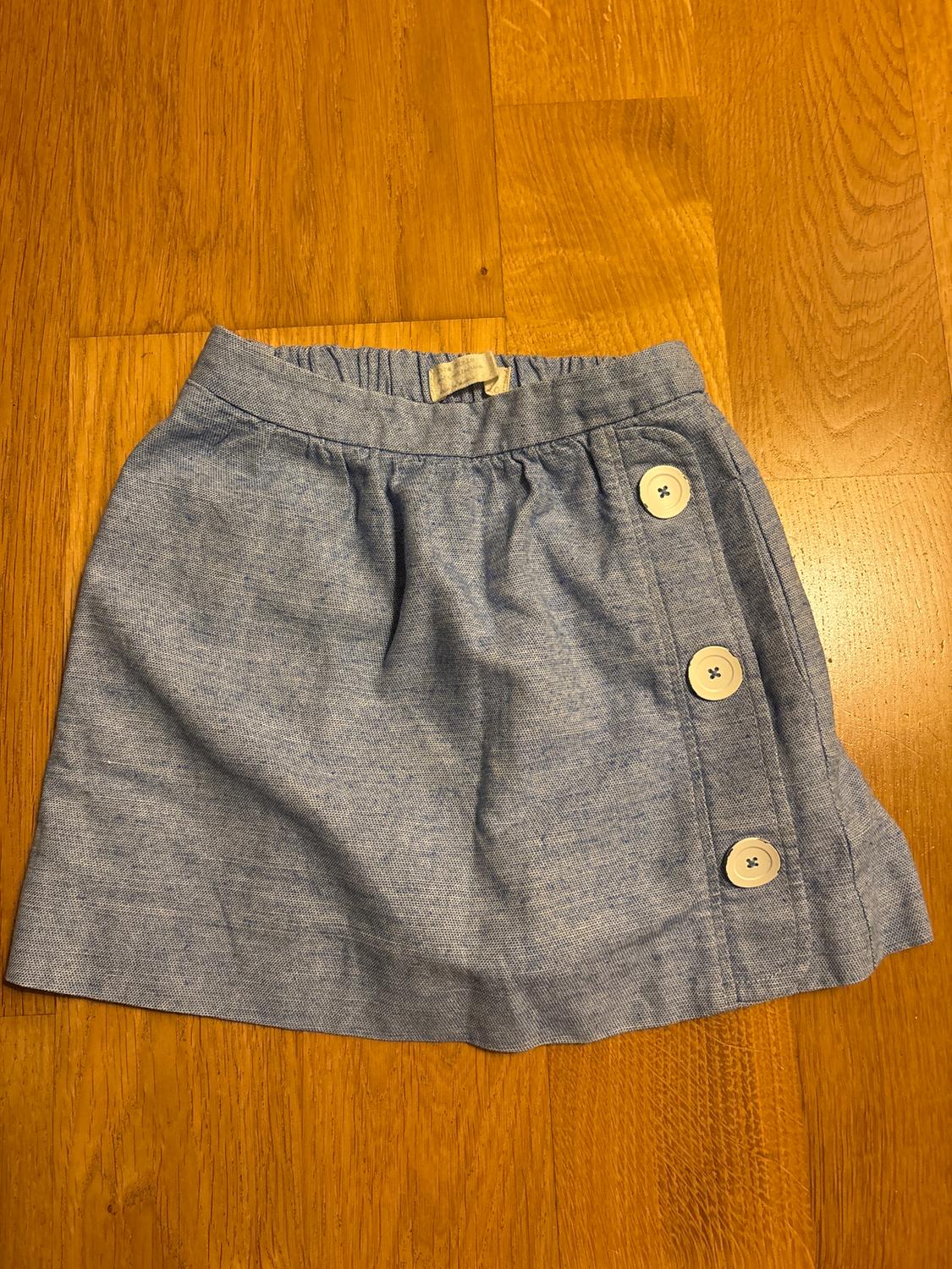 Light blue short skirt with white buttons on the side, on a wooden floor.