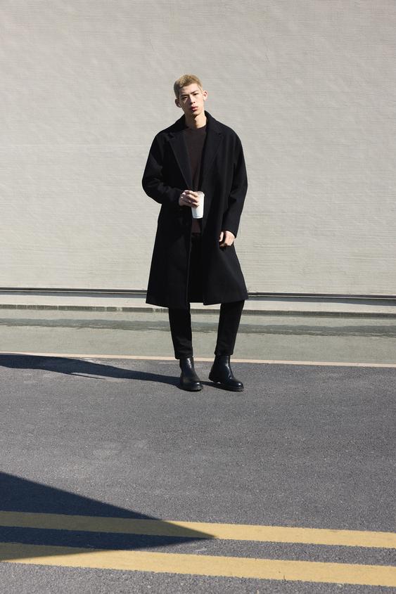 Long black coat, dark jumper, black trousers and black boots.