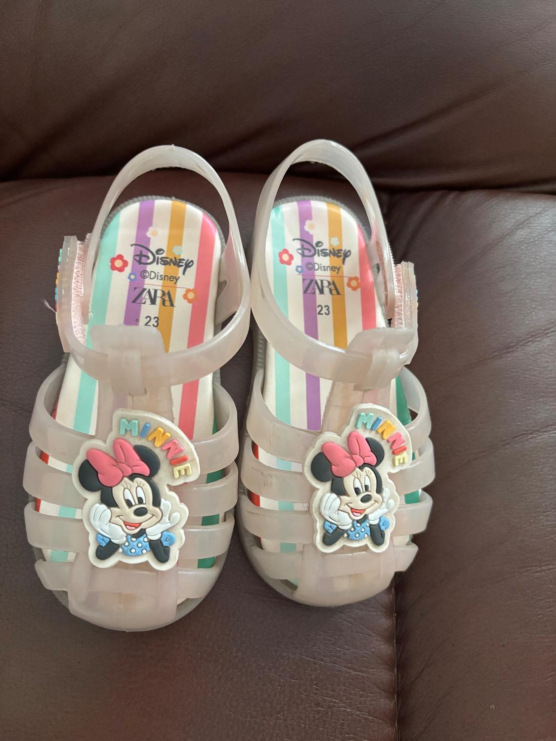 Transparent children's sandals with Minnie Mouse design and multicolored striped insole. Visible text: "Disney", "ZARA", "23".