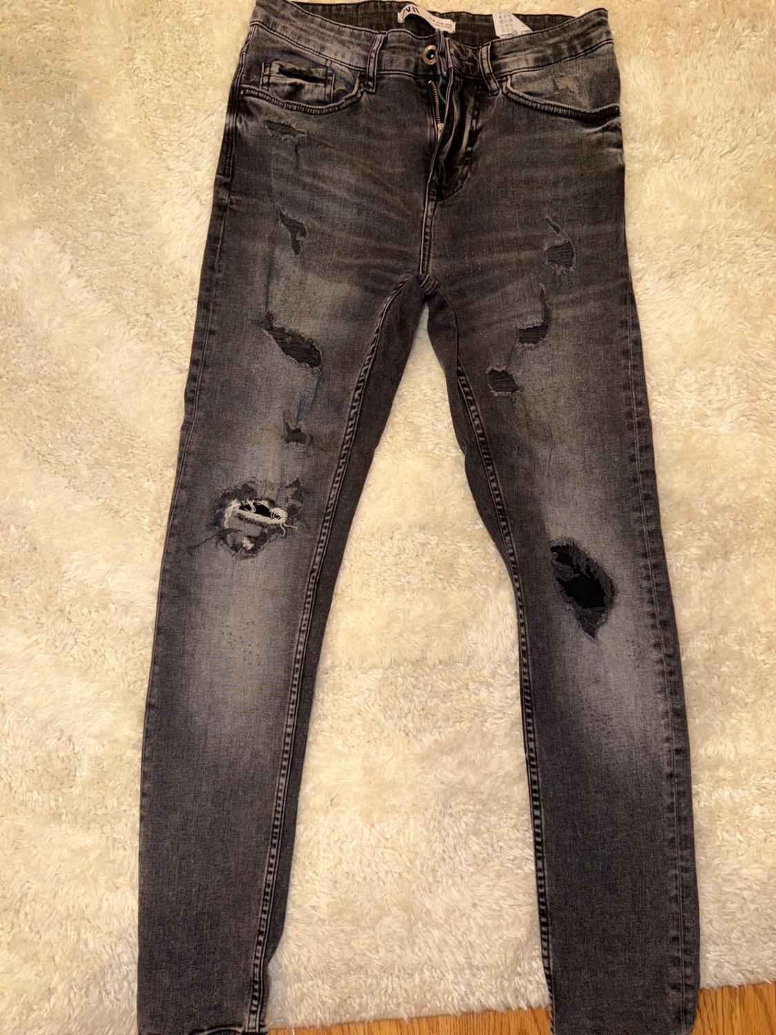 Dark grey ripped and washed-effect jeans, on a white shag pile rug. Label with ZARA text. Casual style.
