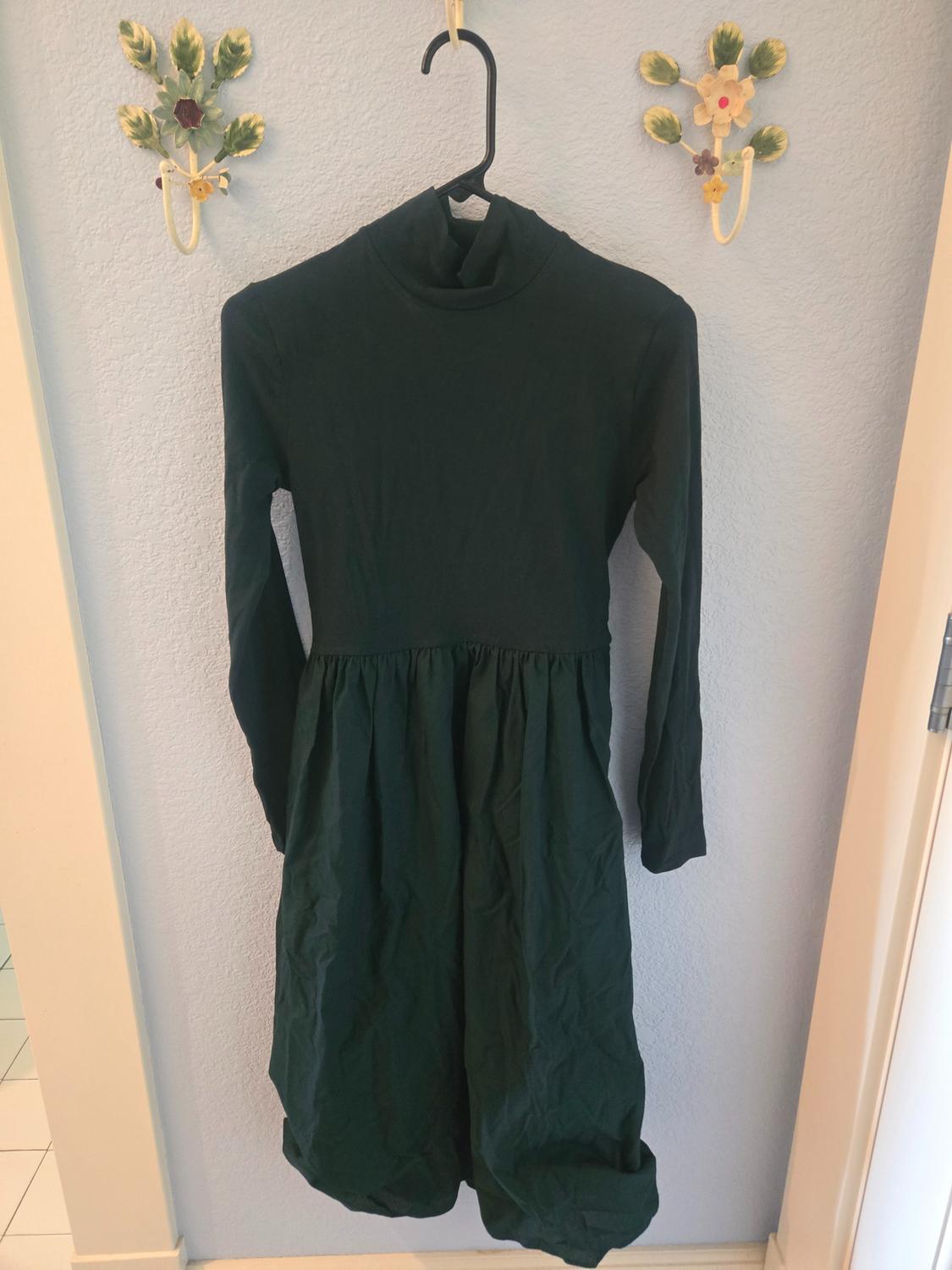 Dark green long-sleeved dress hanging on a black hanger against a light blue wall, decorated with floral hooks.