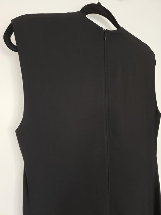 Sleeveless black dress hanging on a hanger, viewed from the back, showing a central zip. White background.