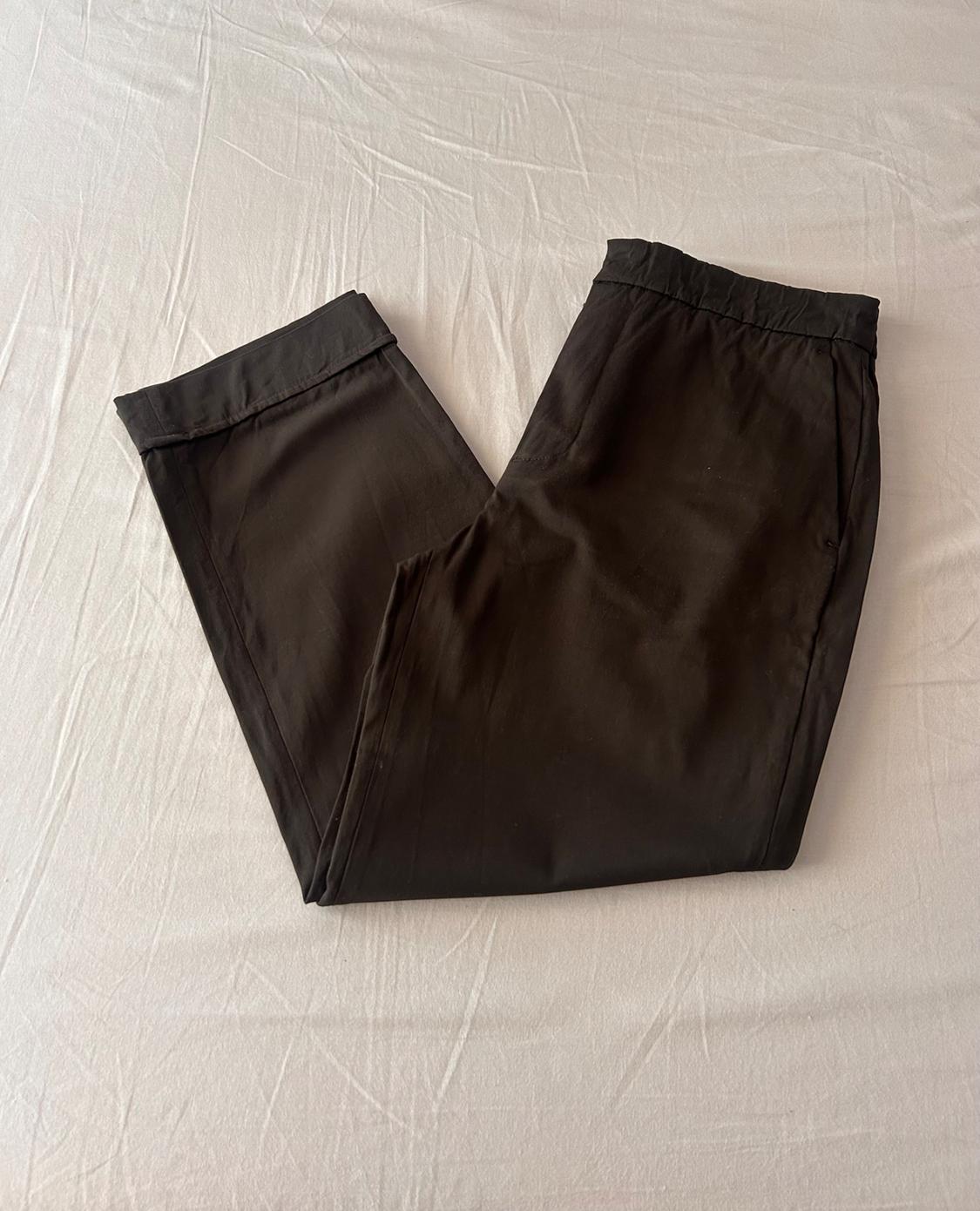 Dark trousers with an elasticated waist and turn-up hems, folded in half on crumpled white fabric for a casual and relaxed style.
