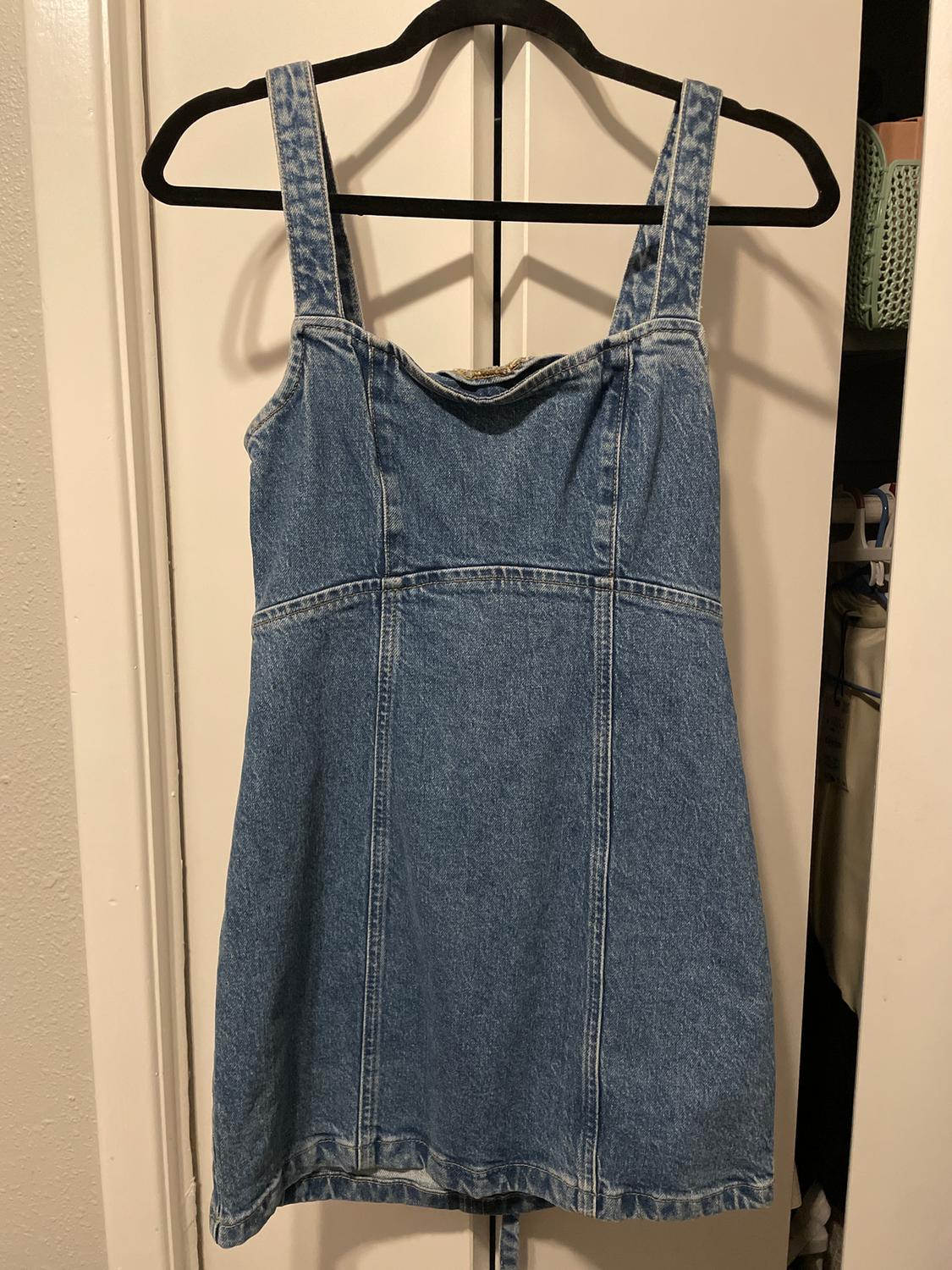 Sleeveless blue denim dress hanging on a black hanger, with visible stitching and a white door in the background.