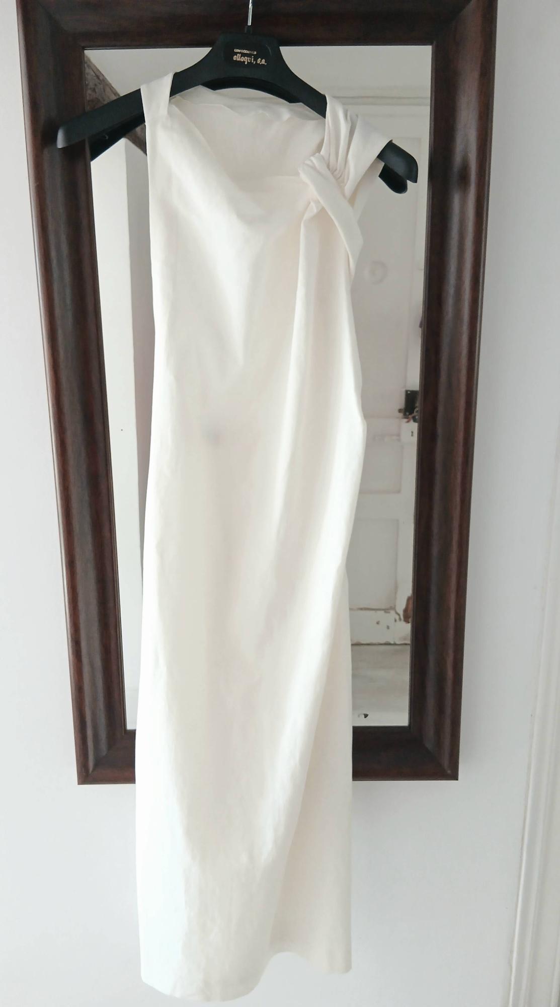 White dress hanging on a black hanger in front of a mirror with a wooden frame. The hanger has the text "elago, s.a.".