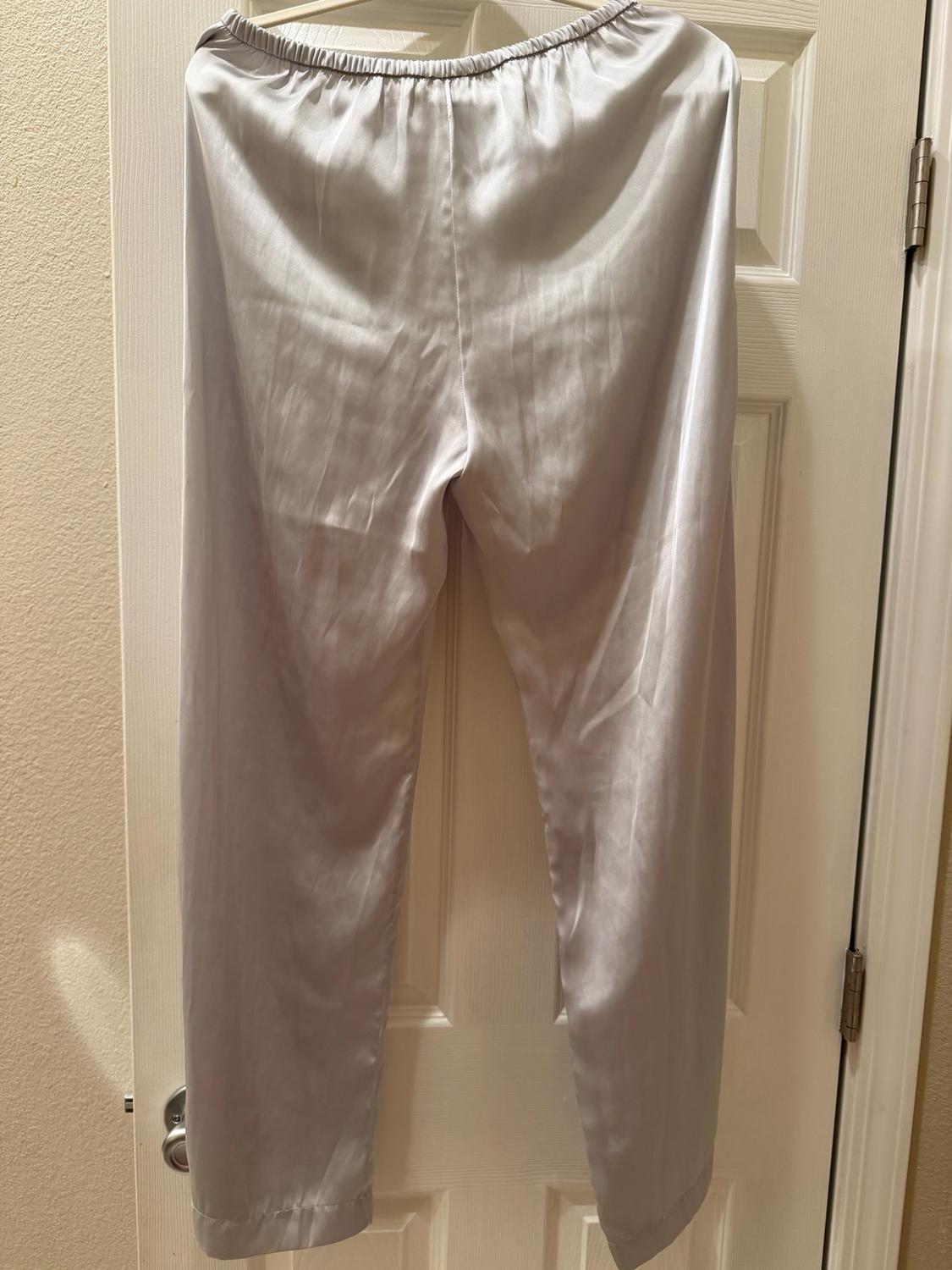 Light gray satin-finish fluid trousers with an elastic waistband, hanging on a white door.