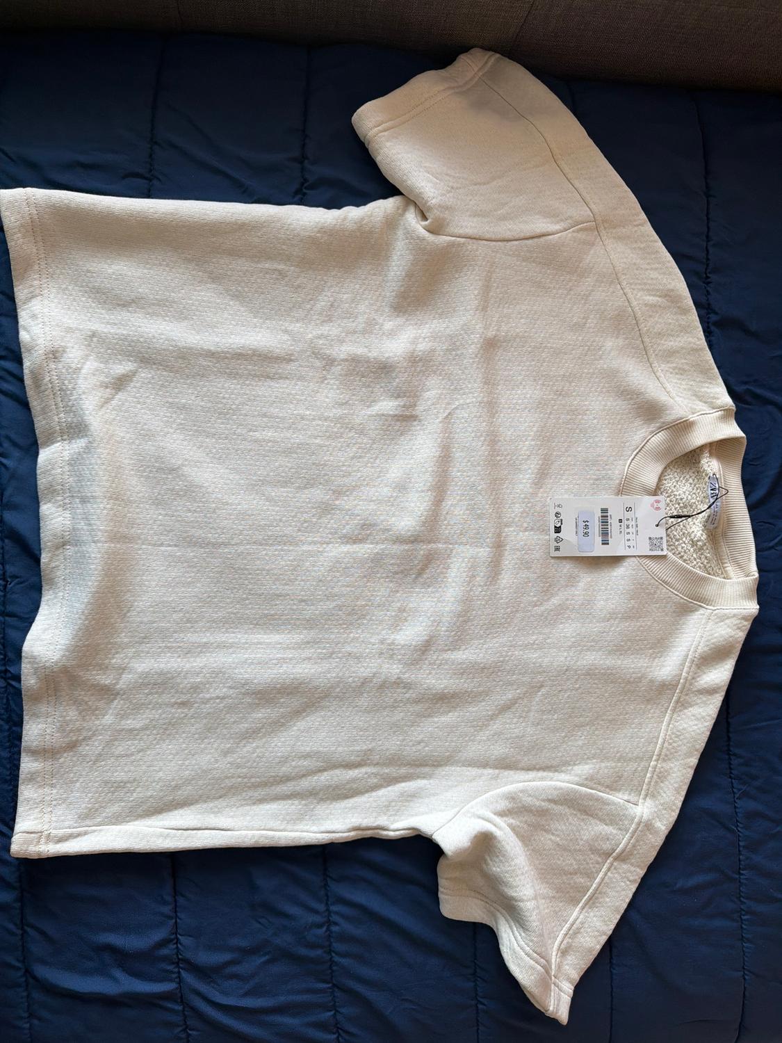 White short-sleeved T-shirt on a blue bedspread, with a visible label on the collar.
