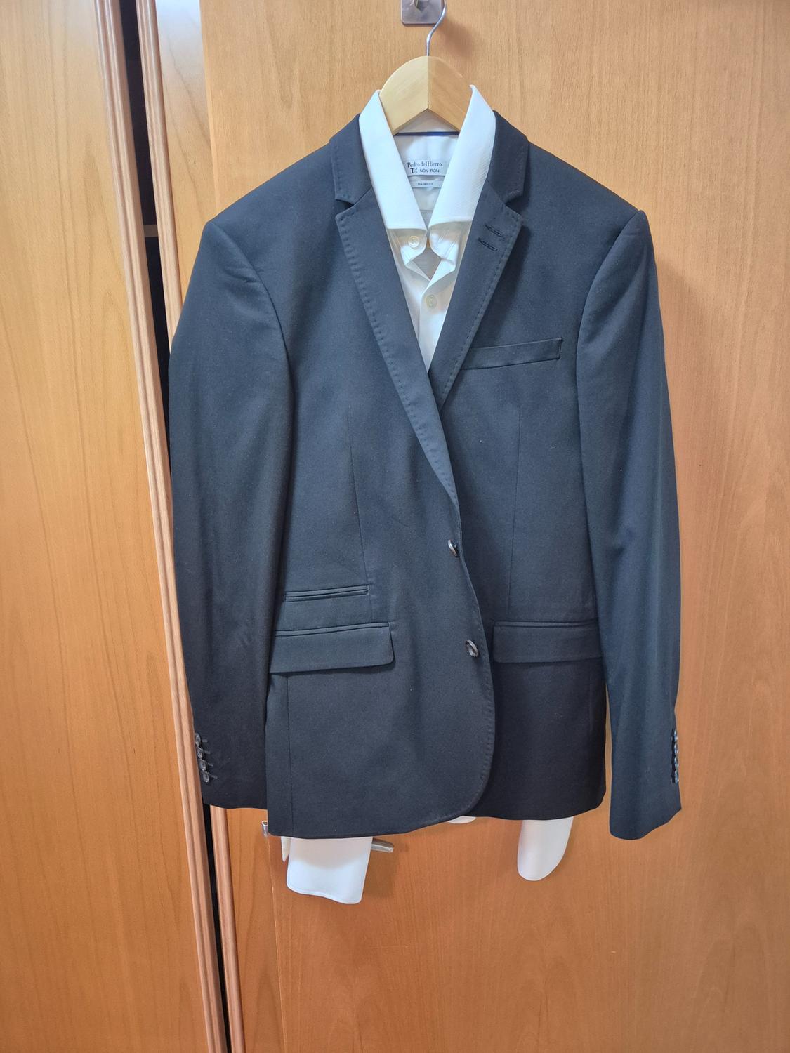 Black jacket with white shirt hanging on a wooden hanger over a light wooden door.