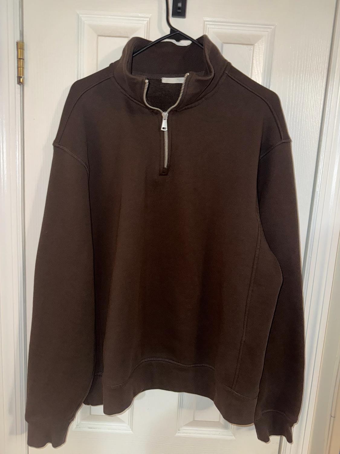 Brown long-sleeve sweatshirt with a half-zip, hanging on a black hanger on a white door.