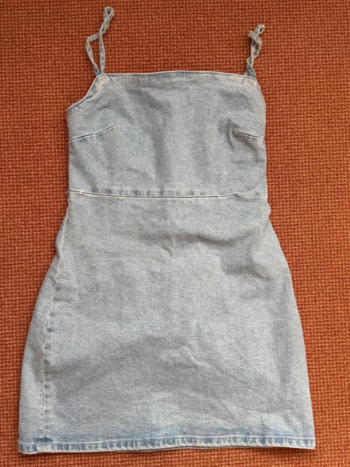 Light blue denim mini dress with thin straps on a textured orange background.
