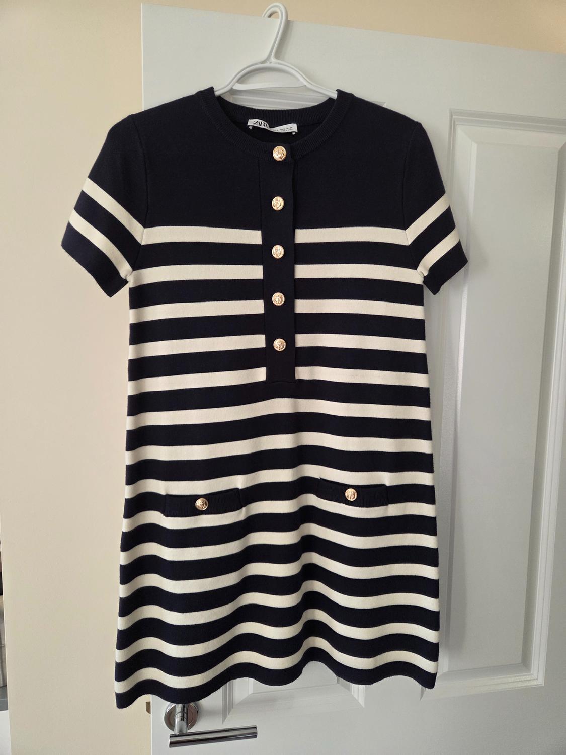 Short striped knit dress in white and navy, short sleeves, gold buttons and pockets. ZARA label. Hung on a white door.
