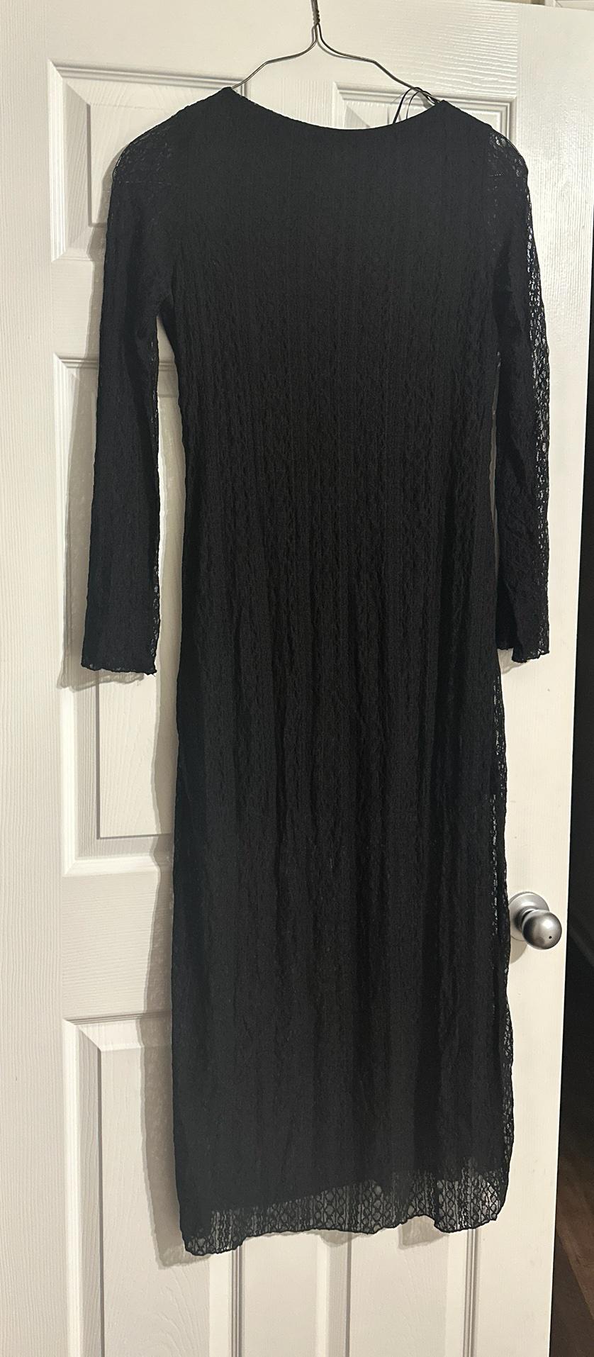 Black lace dress with sheer detailing and long sleeves, hanging on a hanger on a white interior door with a silver knob.