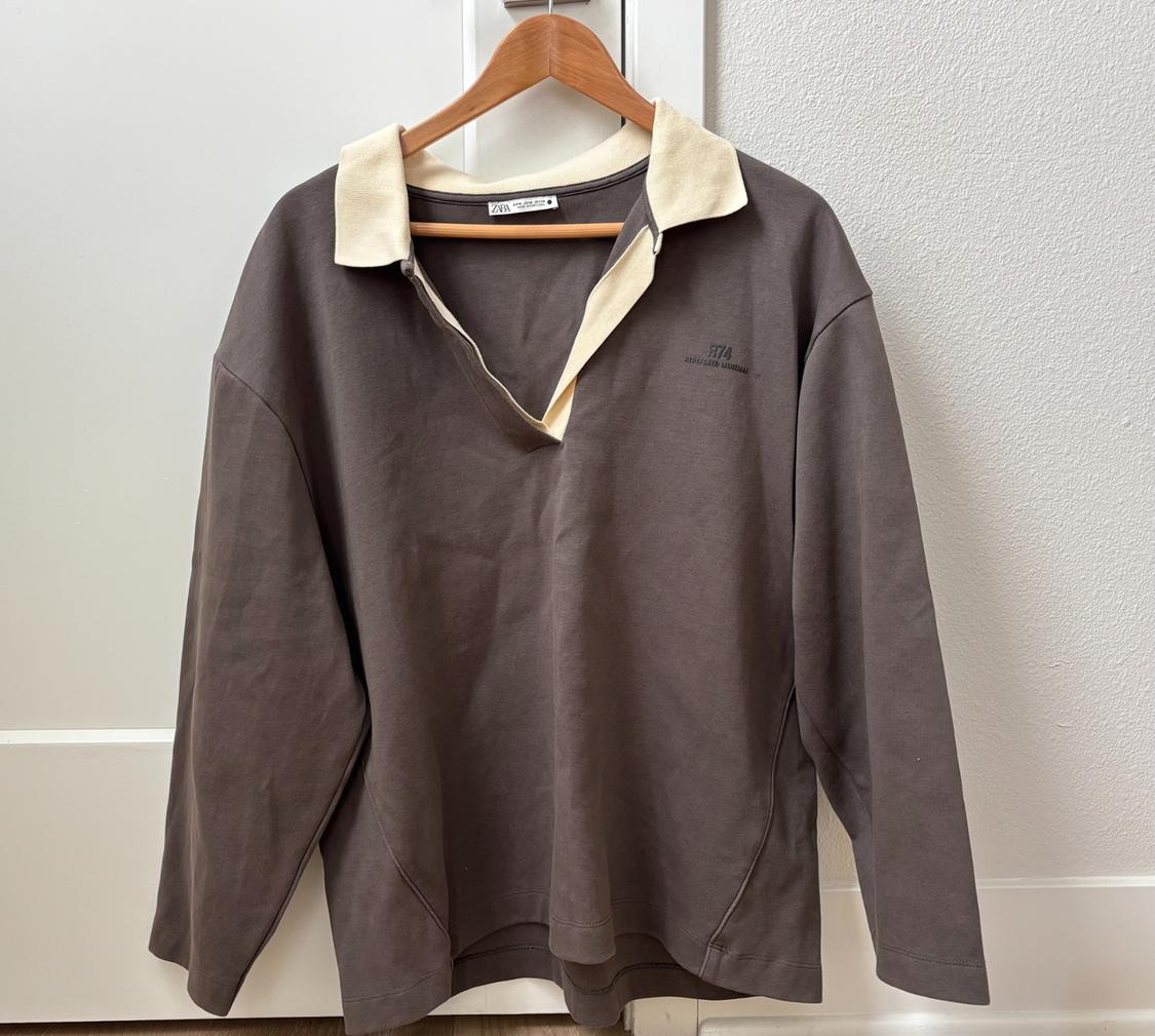 Brown long-sleeve T-shirt with a cream collar, hanging on a wooden hanger over a white door. Includes the text "R74" on the chest.