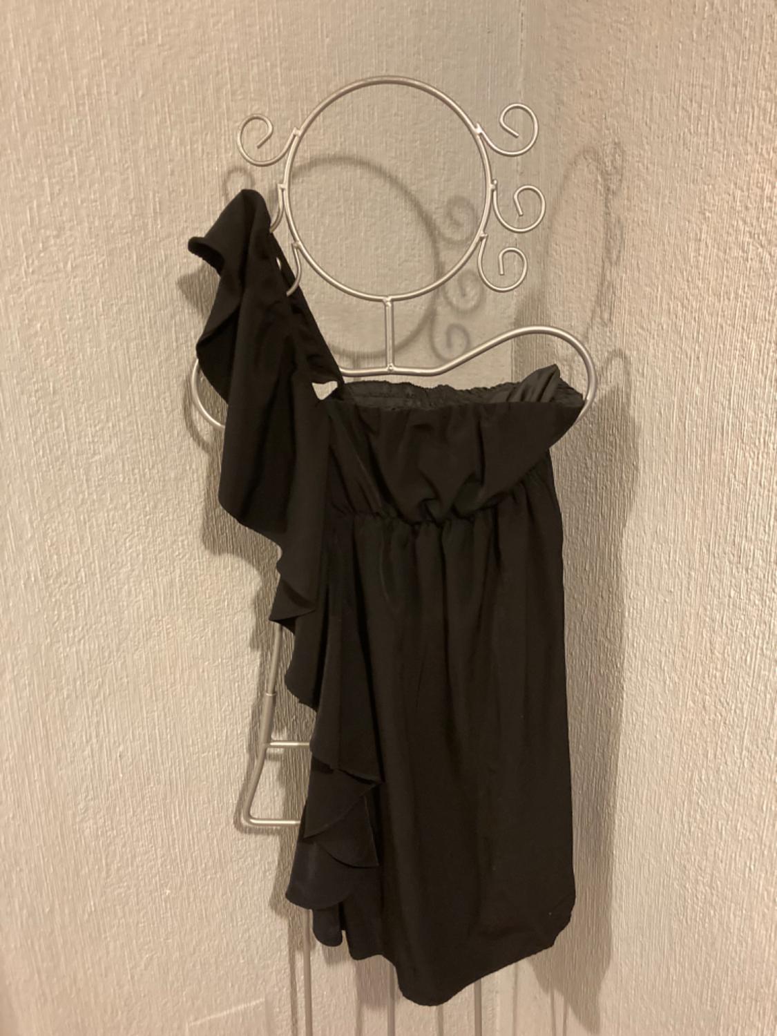 Front view of a black dress with one strap and ruffles on the shoulder.
