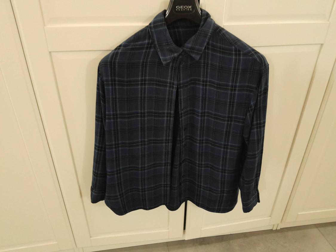 Dark blue checked shirt hanging on a black hanger with the "GEOX" brand visible, against a background of white doors.