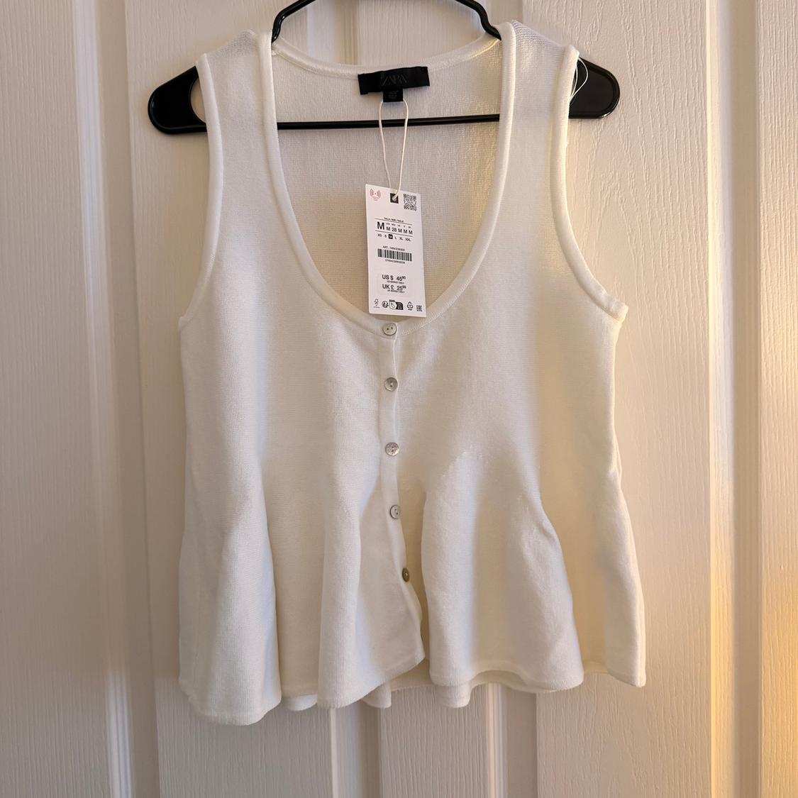 Sleeveless white blouse with front buttons, hanging on a black hanger. Visible tag with size and price details.