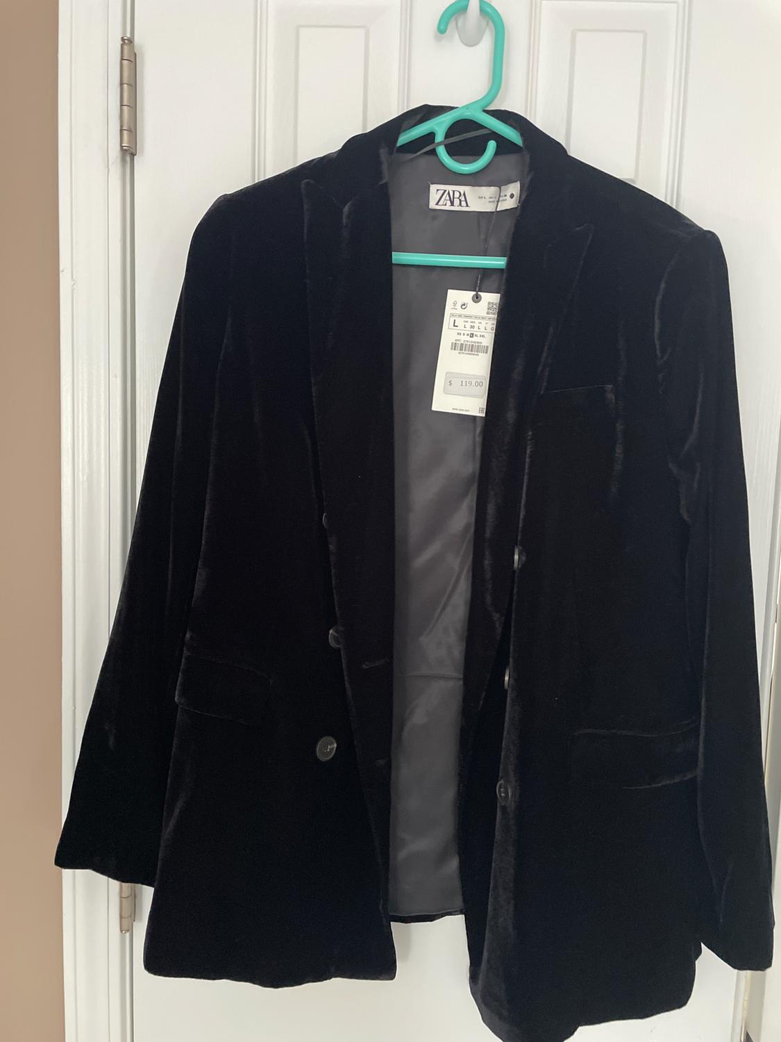 Black velvet jacket hanging on a green hanger. Visible tag with a price of $119. White door in the background.