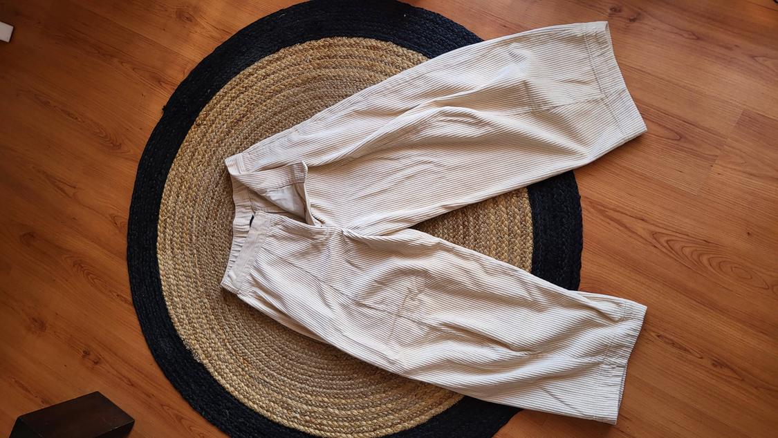 Fine-striped beige trousers on a circular jute rug on a light wooden floor.
