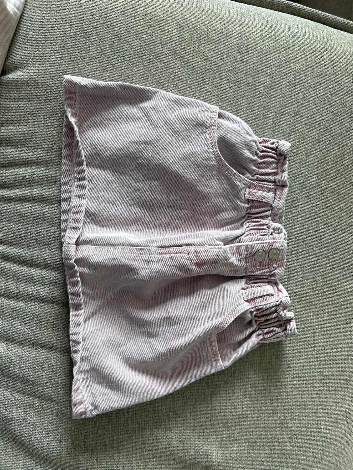 Light pink denim shorts with an elasticated waist and buttons, on a grey fabric background.
