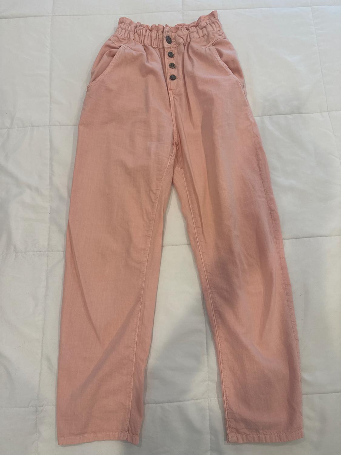 Light pink fabric pants with a ruched elastic waistband and dark buttons, on a white bedspread.
