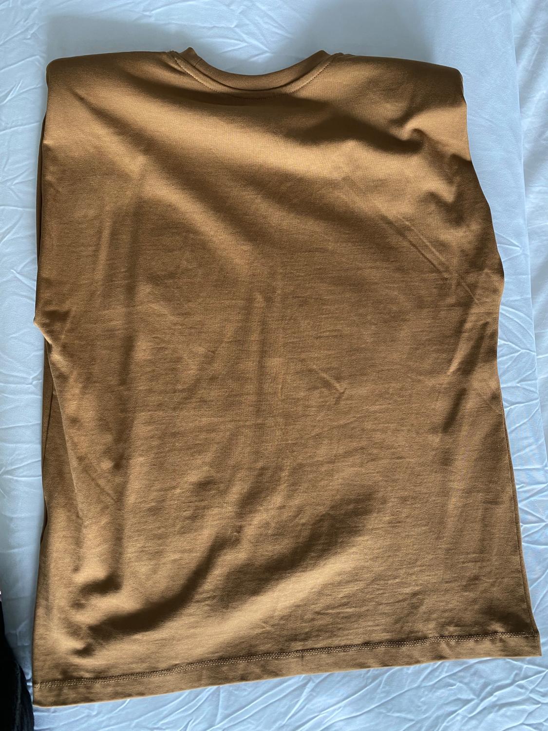 Light brown T-shirt, short-sleeved, placed on a white surface with a wrinkled texture.