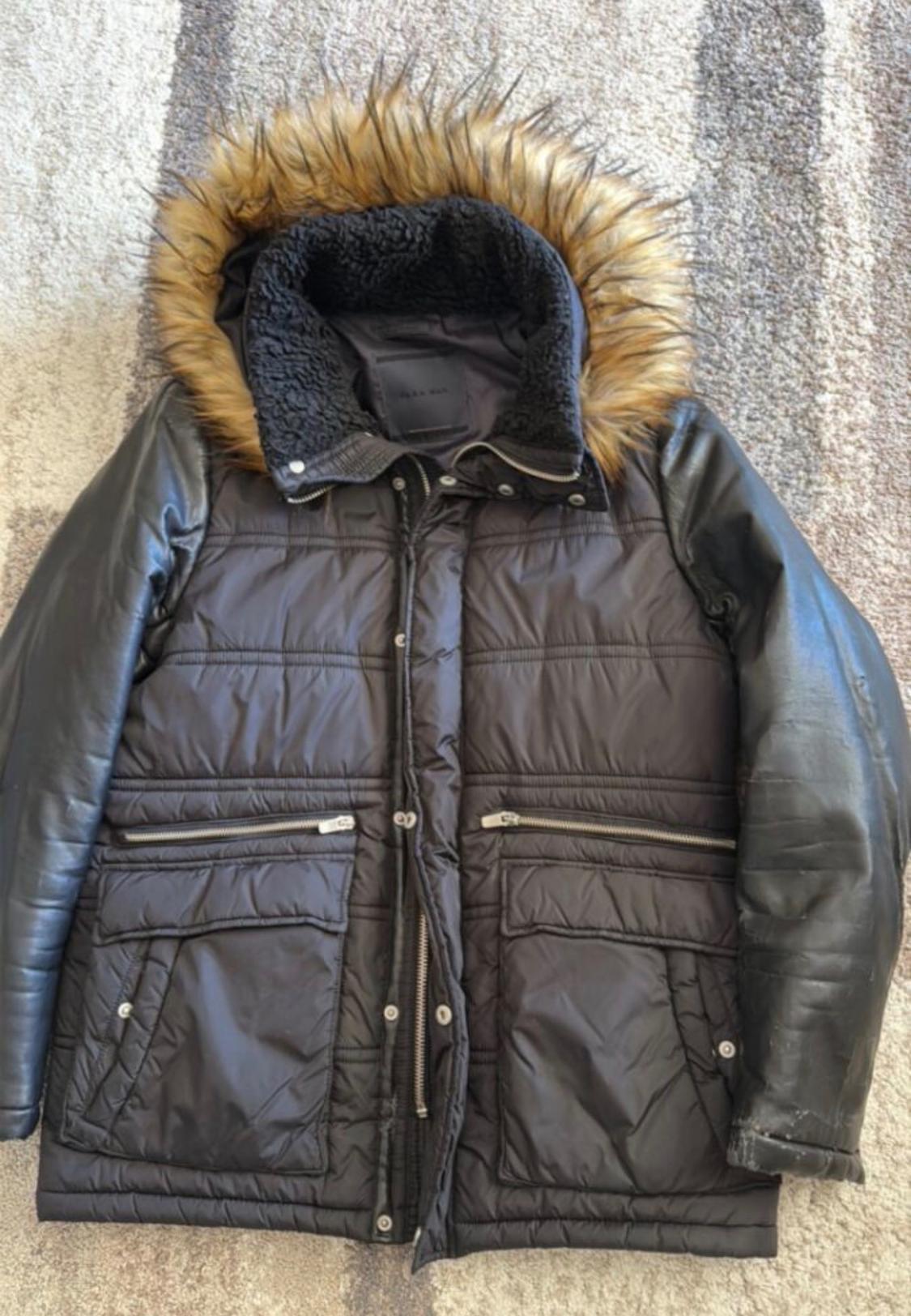Black padded jacket with brown faux fur hood and leather sleeves. Pockets with zips and buttons.