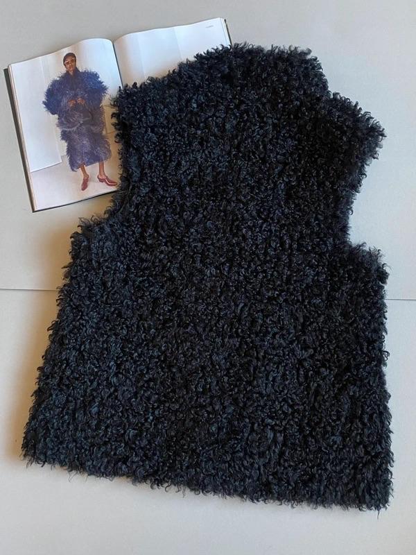 Black fluffy textured gilet on a table next to an open magazine showing a model in a similar coat.