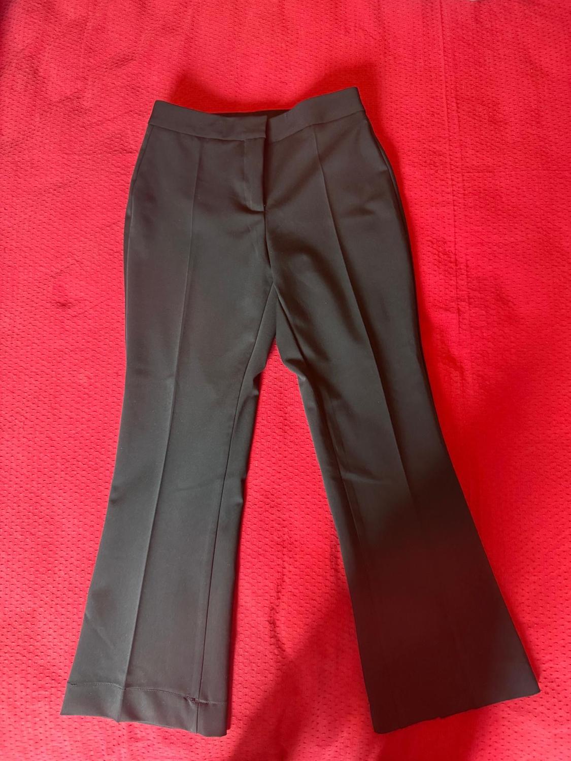 Black dress trousers with a front crease, laid out on a red fabric background. Relaxed-style flat lay composition.