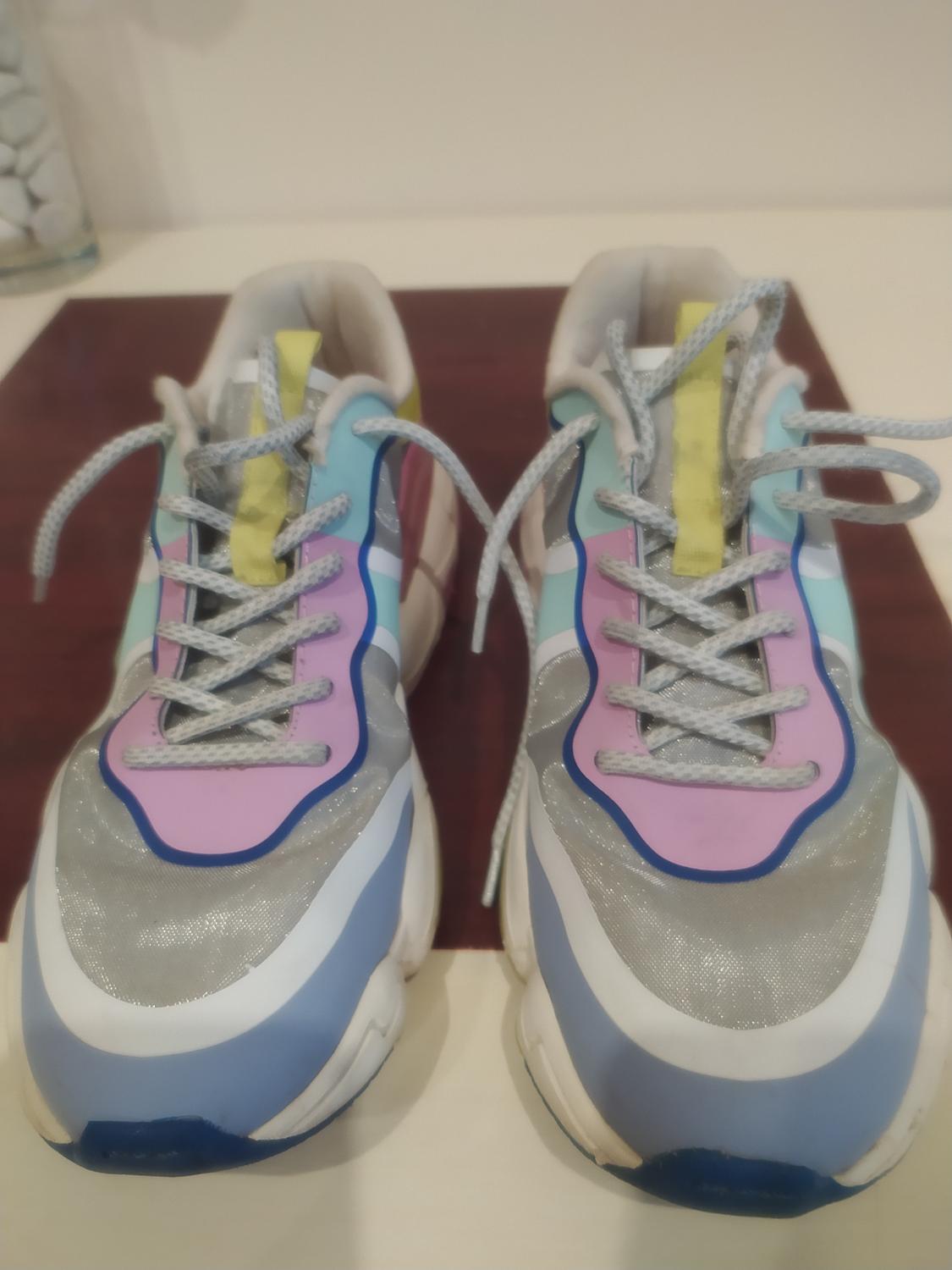 Grey lace-up trainers, with pink, blue, and yellow details, on a wooden surface.