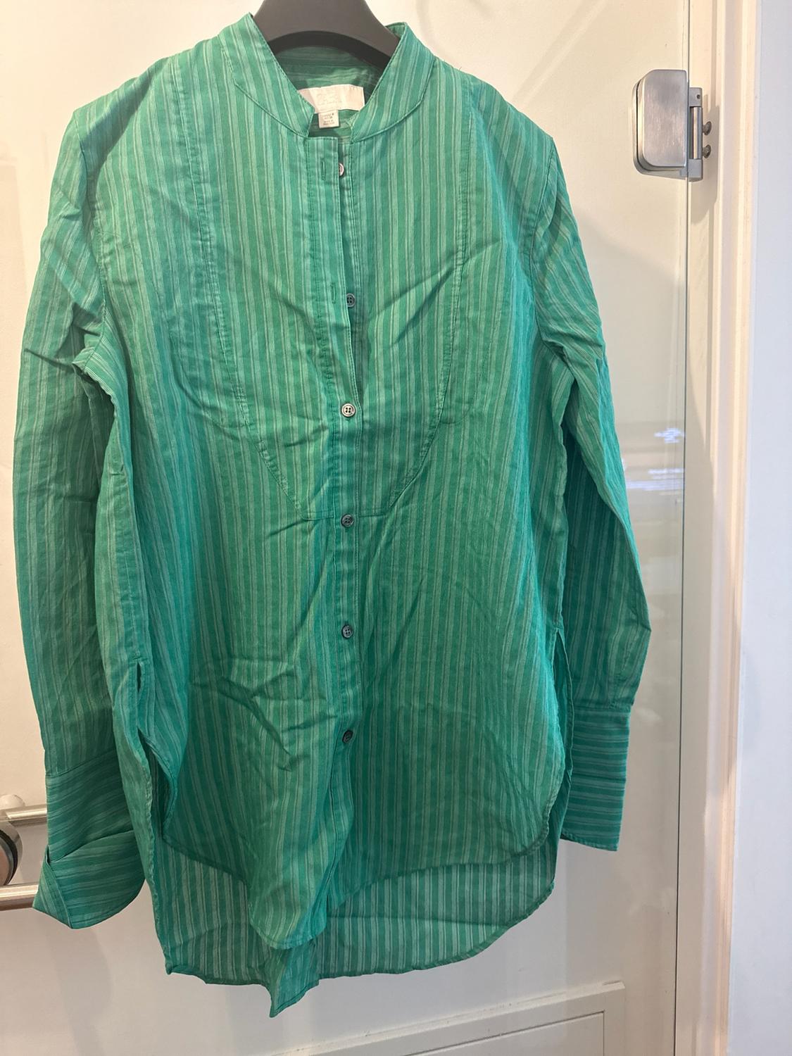 Green shirt with vertical stripes and long sleeves, a mandarin collar, hanging on a black hanger on a white door.