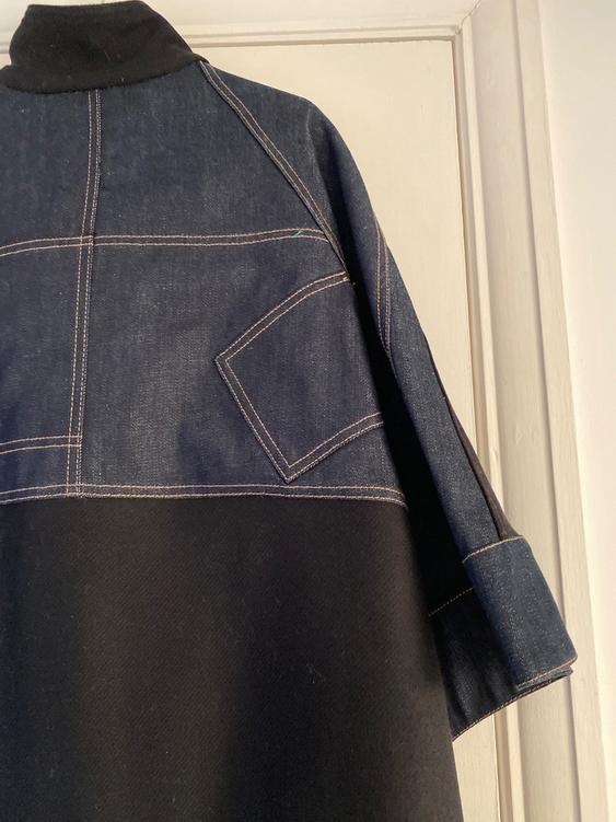 Blue denim jacket with visible stitching and a back pocket, hanging on a white door.