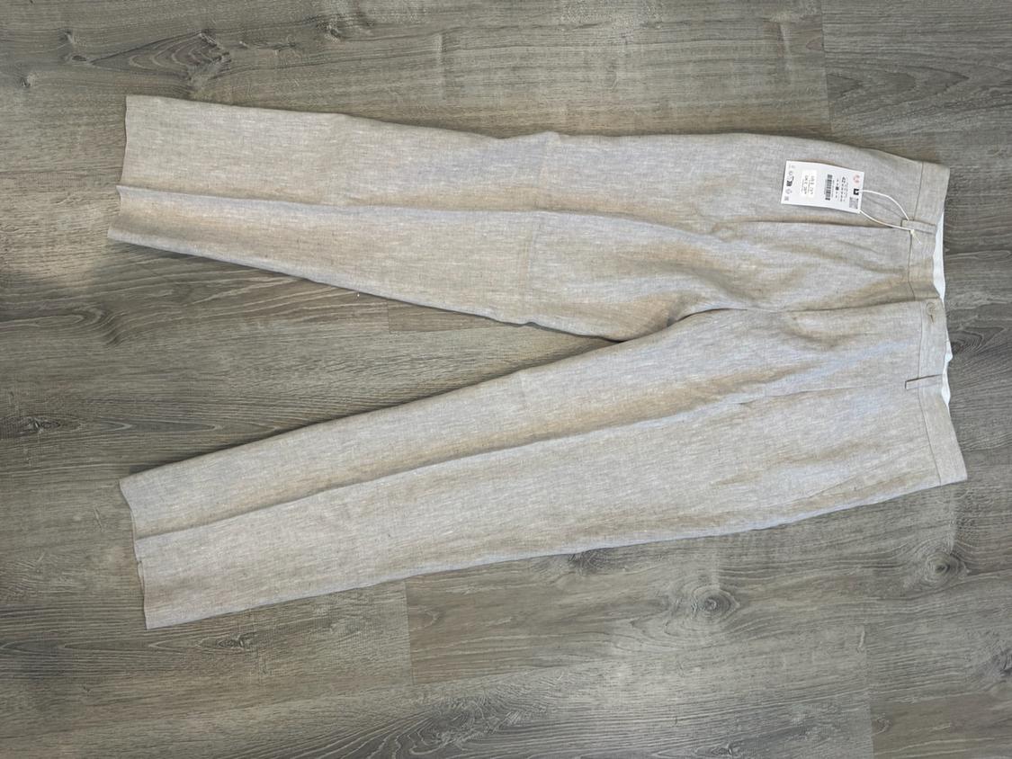 Light beige trousers with a tag, laid flat on a wooden floor.