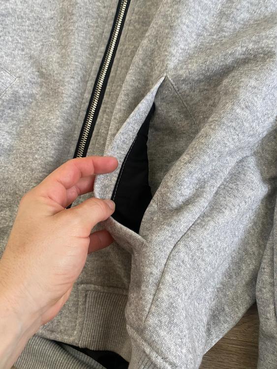 Hand opening the pocket of a gray jacket with a black zipper on a wooden surface.