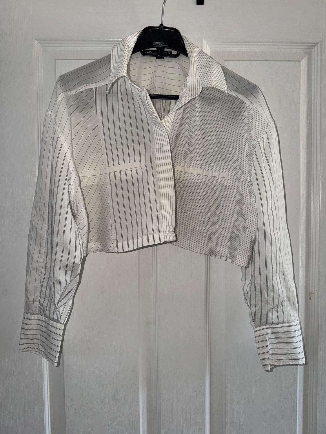 Short black and white vertical striped shirt hanging on a black hanger in front of a white door.