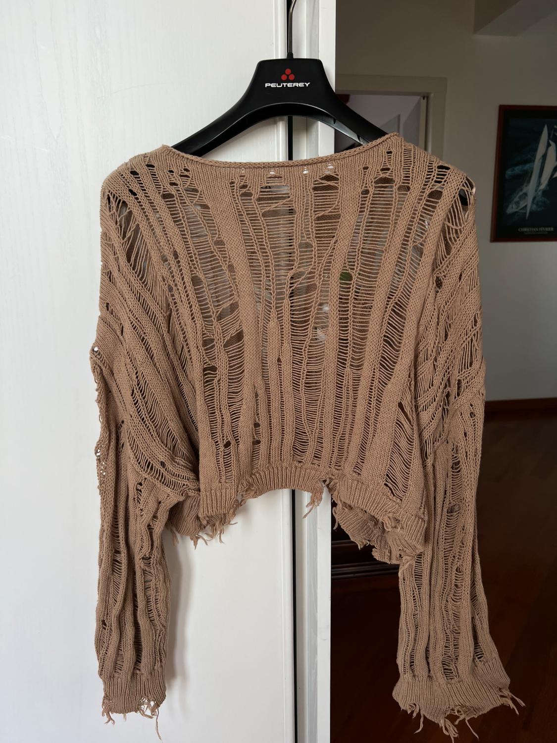 Brown knitted jumper with distressed detailing and holes, hanging on a black hanger with "PEUTEREY" logo, against a white door background.