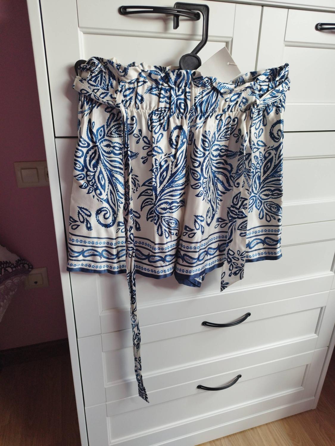 White shorts with a blue pattern hanging on a black hanger in front of a white wardrobe.